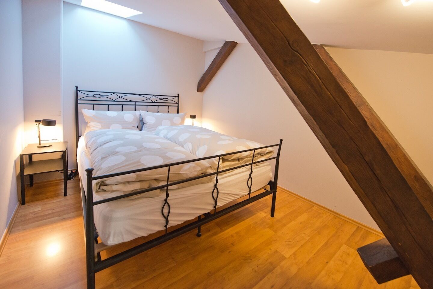 Een slaapkamer met een bed, nachtkastjes en een schuine plafond.