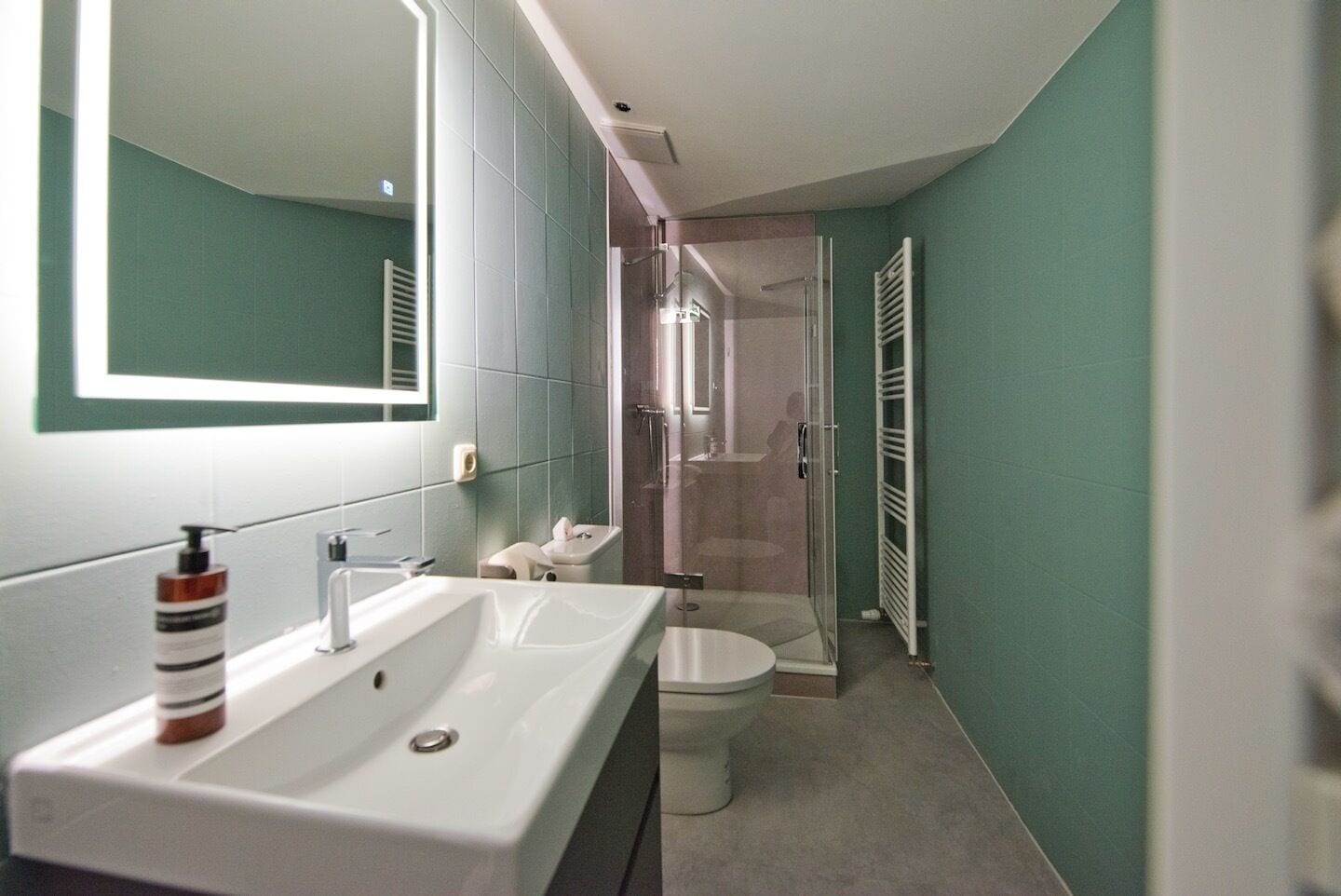 Un baño moderno con un espejo grande, dos lavamanos, un inodoro y una zona de ducha.