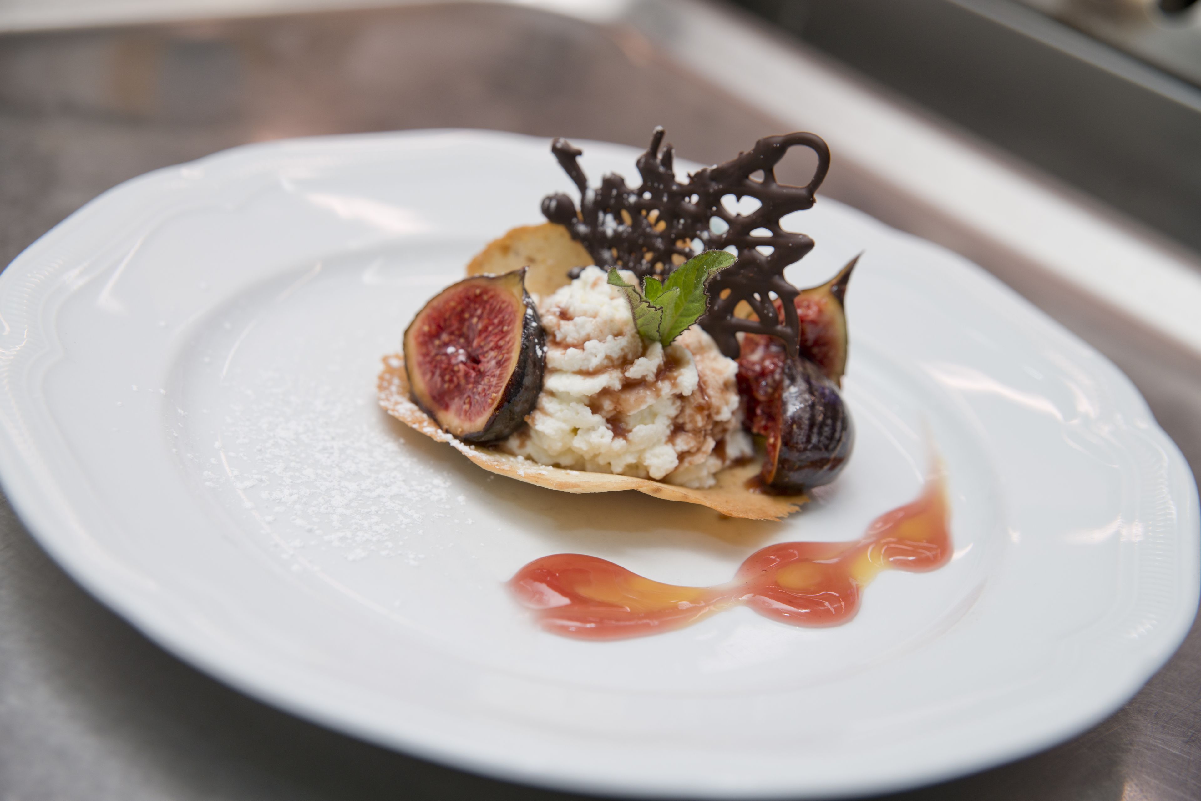 Un dessert servi dans une assiette blanche, agrémenté d’un décor en chocolat et d’une feuille de menthe.