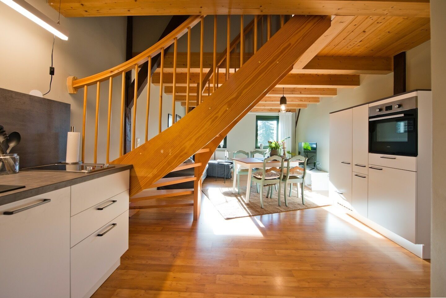 Une cuisine moderne avec un plancher en bois, un four encastré et un coin repas comprenant une table et des chaises.