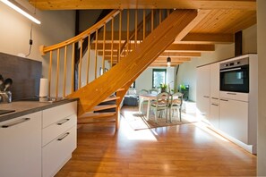 Una cocina moderna con piso de madera, horno empotrado y comedor con mesa y sillas.
