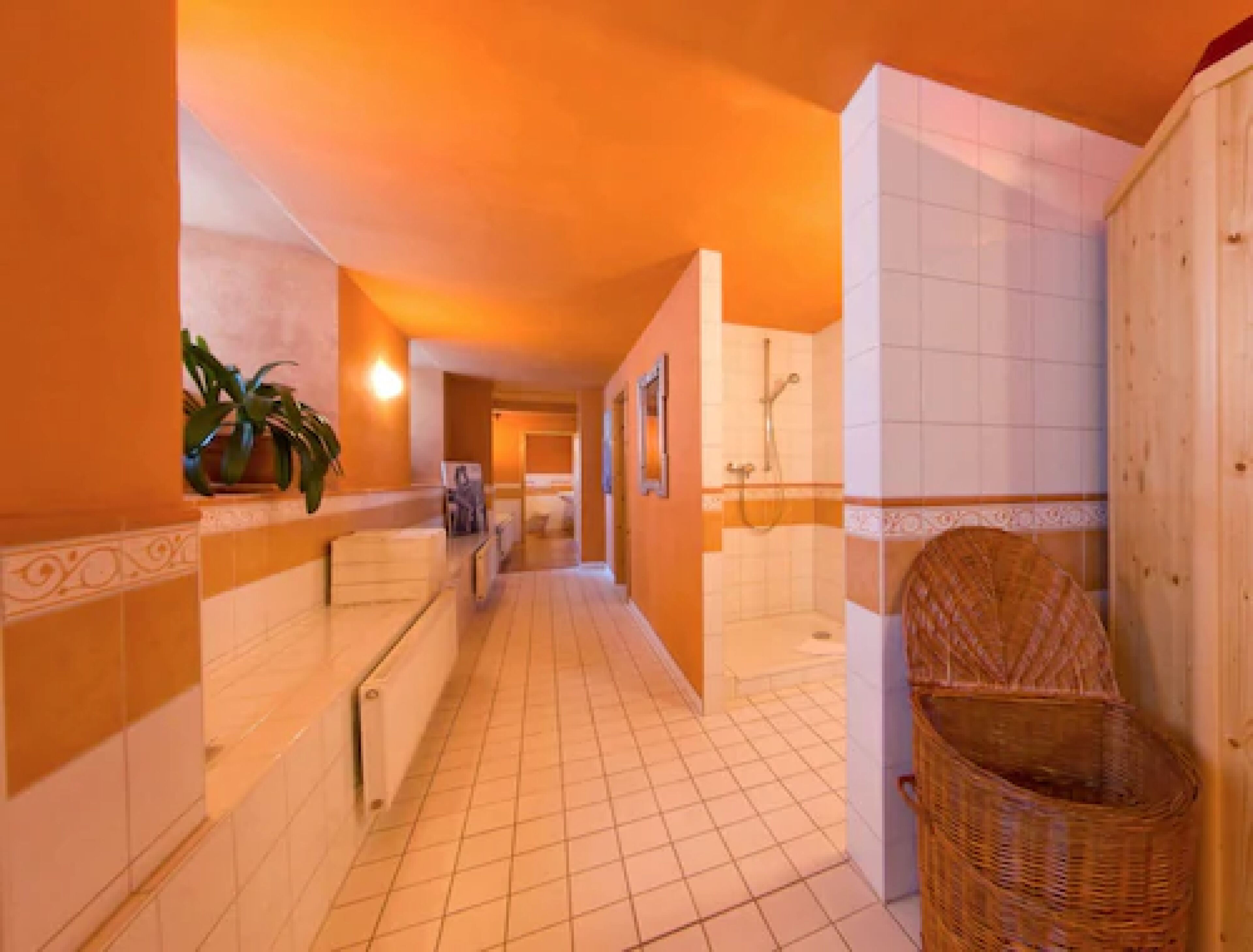 Pasillo de hotel con pisos de baldosas, un radiador, una silla de mimbre y un área de ducha.