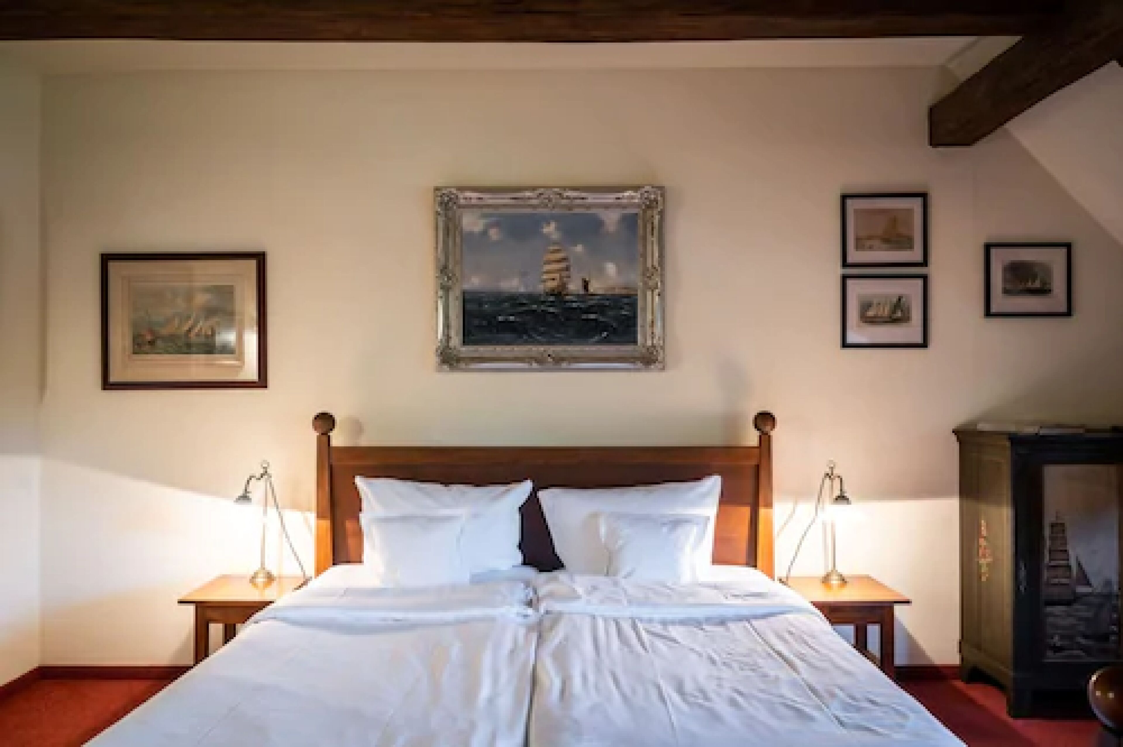 Un lit bien fait, avec du linge de lit blanc, deux tables de chevet avec des lampes et des œuvres d’art encadrées accrochées aux murs.