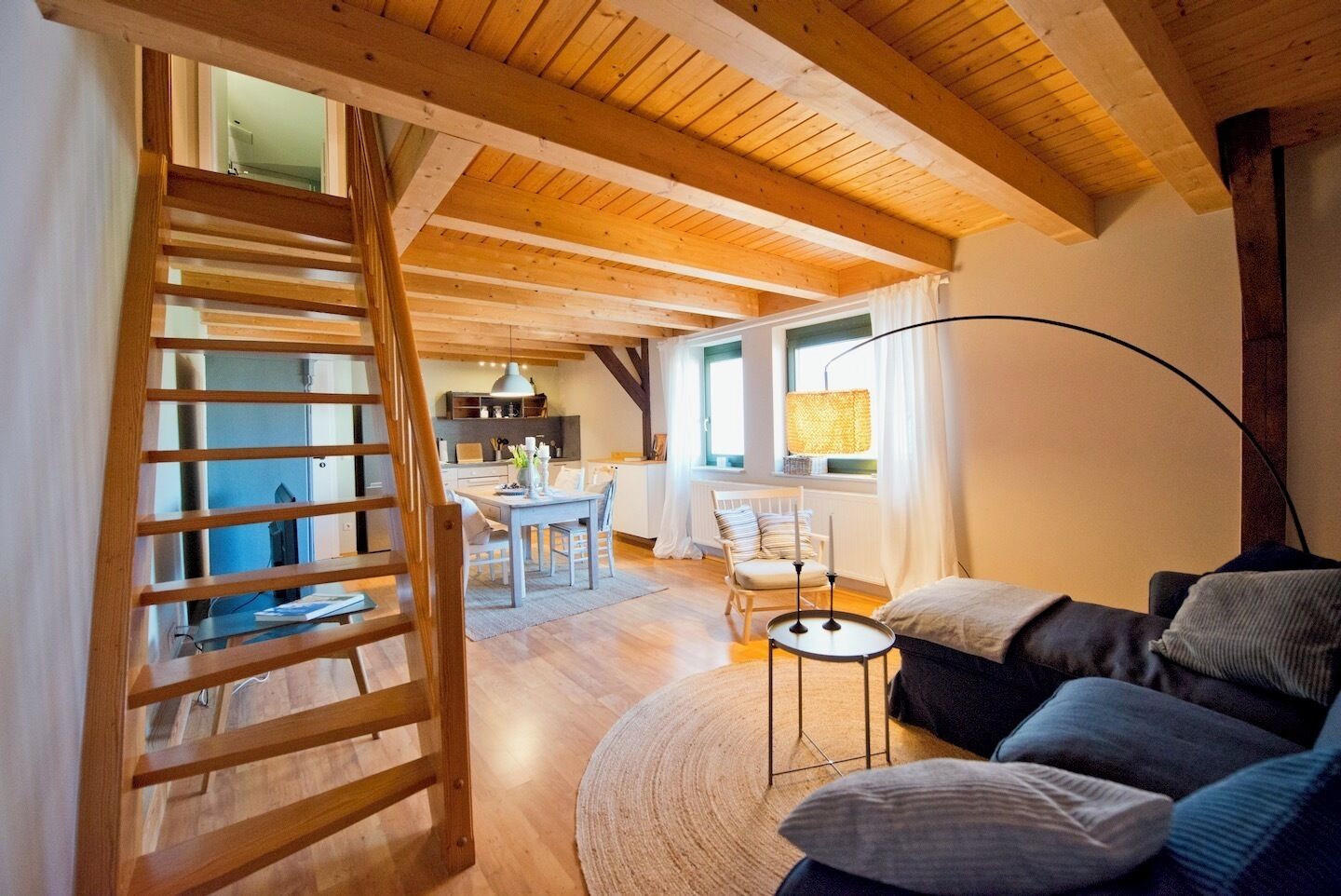 Una sala de estar acogedora con una escalera de madera, un comedor y una cocina al fondo.