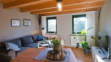 A cozy living room with a wooden ceiling, a sofa, a table with a vase of flowers, and a television.
