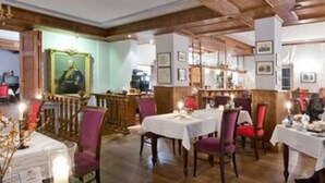 Ein Restaurant mit Holzbalken, Tischen mit weißen Tischdecken und roten Stühlen.