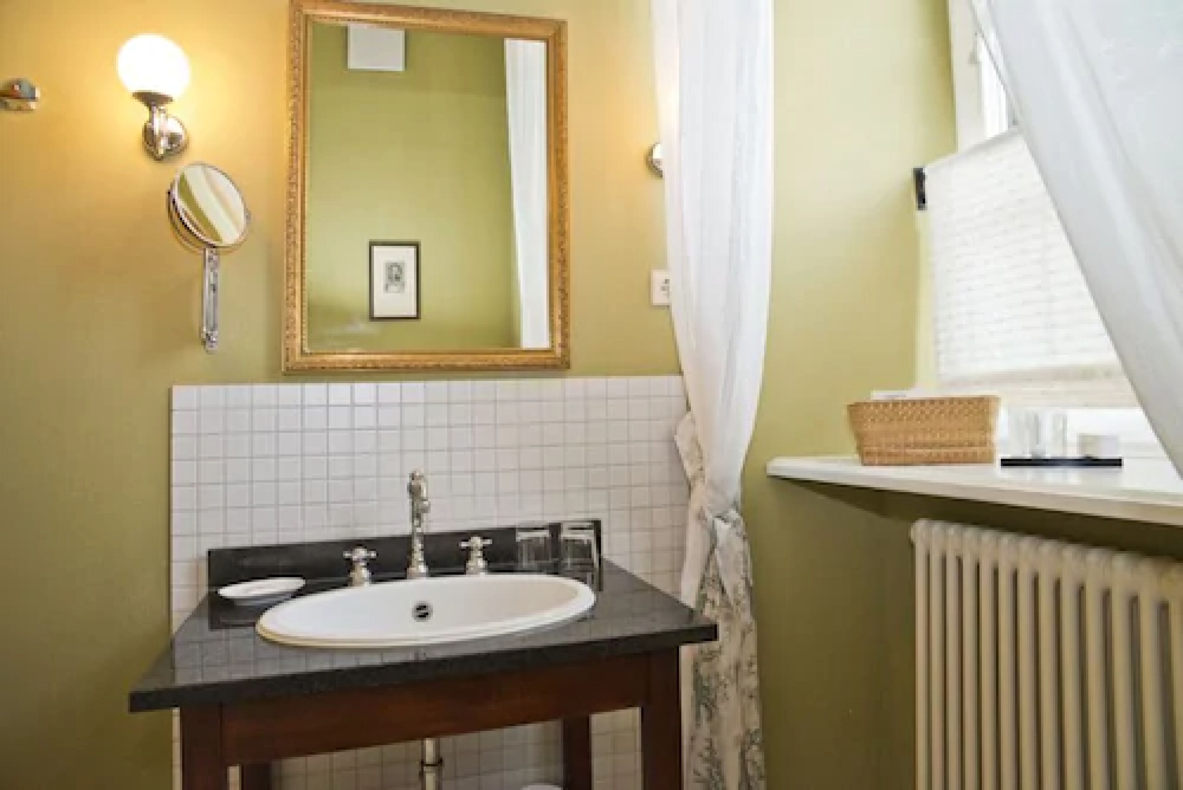 A bathroom with a white sink, a mirror, and a window with a white curtain.
