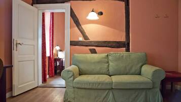 Una habitación con sofá verde, vigas de madera en el techo, una puerta blanca y una cortina roja.