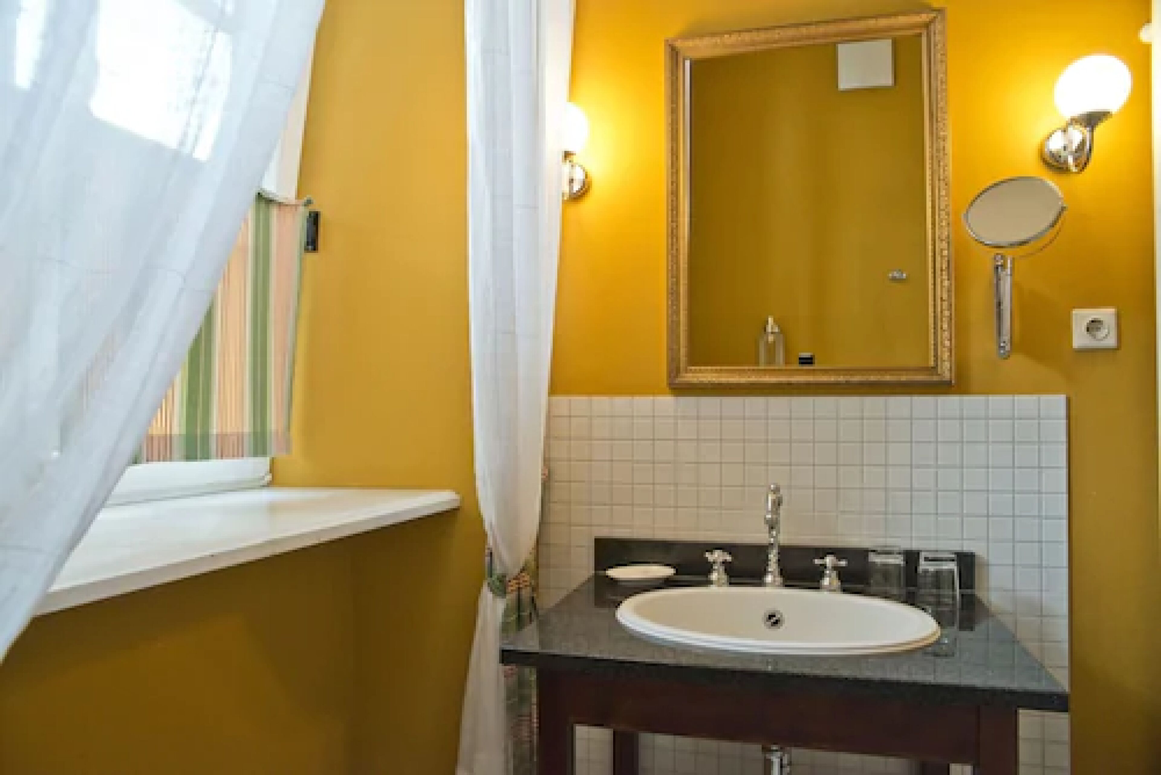 A bathroom with a yellow wall, a white sink, and a mirror.