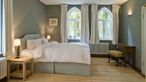 Ein Schlafzimmer mit einem großen Bett, einem Nachttisch mit Lampe, einer Holzbank und einem Fenster mit Vorhängen.