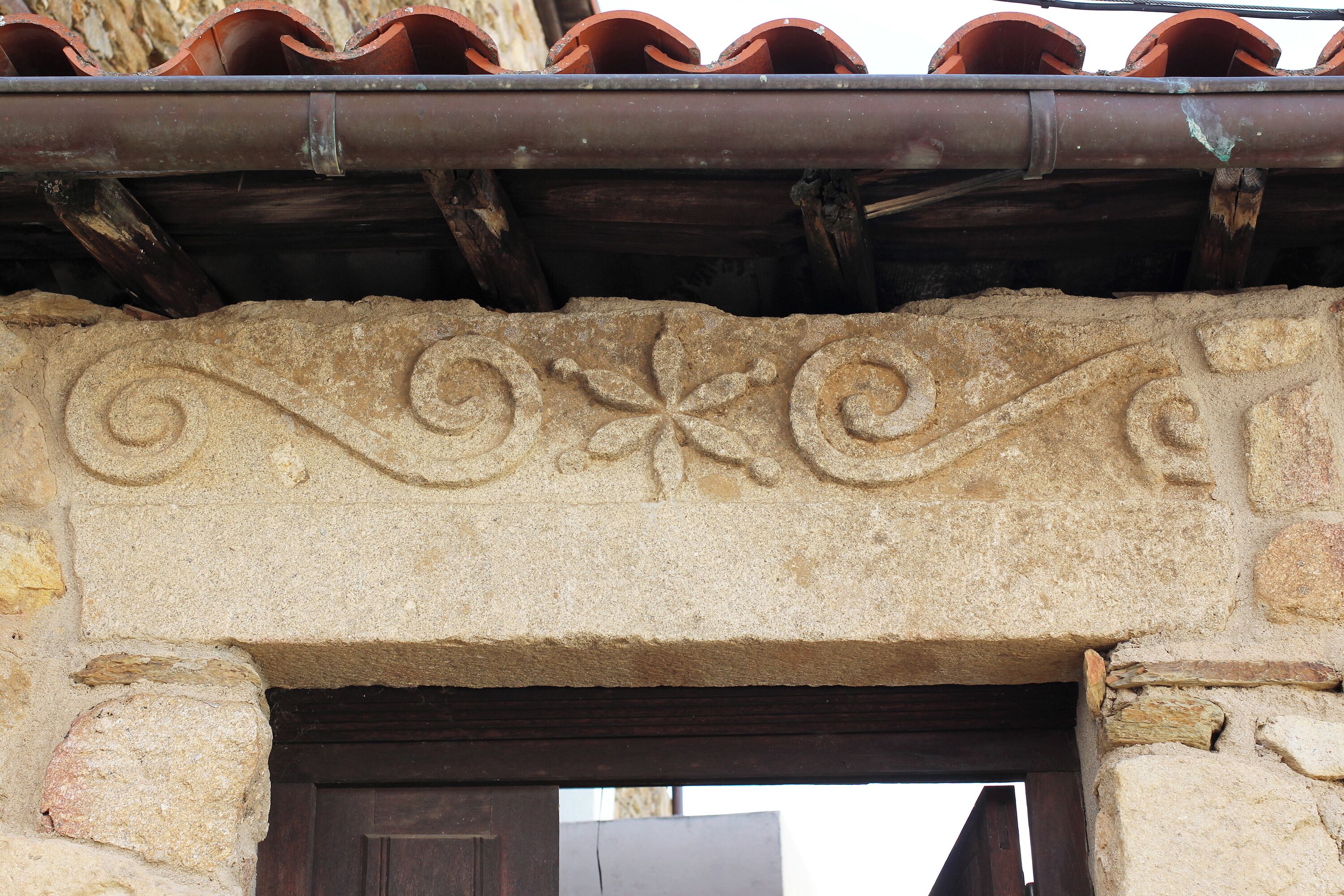 Un arc de pedra amb treballs de talla intricats, una porta de fusta i un teulat de rajoles a la part superior.