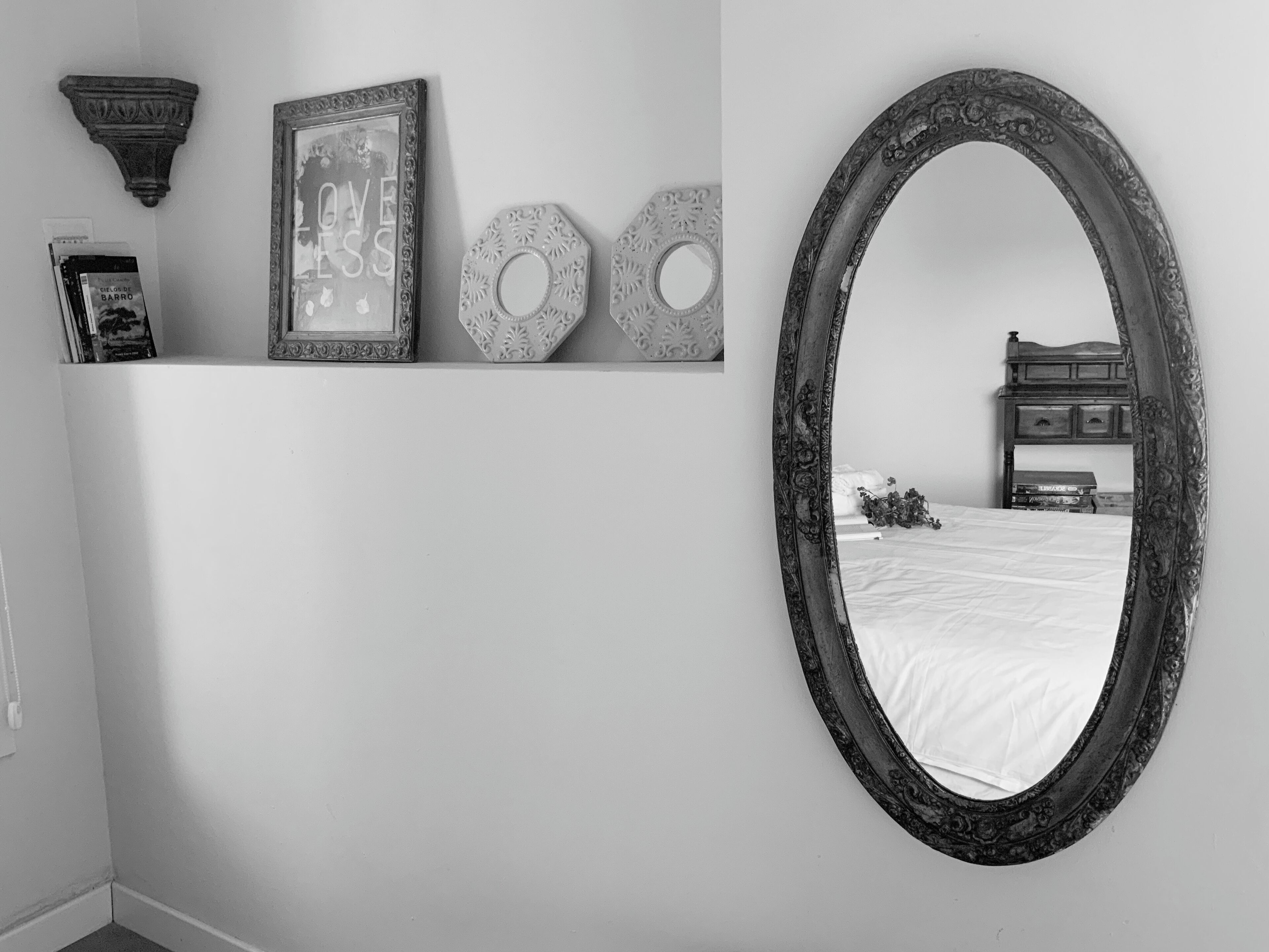 A bedroom with a large ornate mirror, a bed, a nightstand, and a dresser.