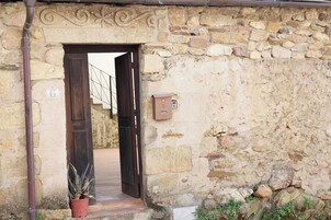 Entrada de un edificio de piedra con puerta de madera, una planta en maceta y un buzón.