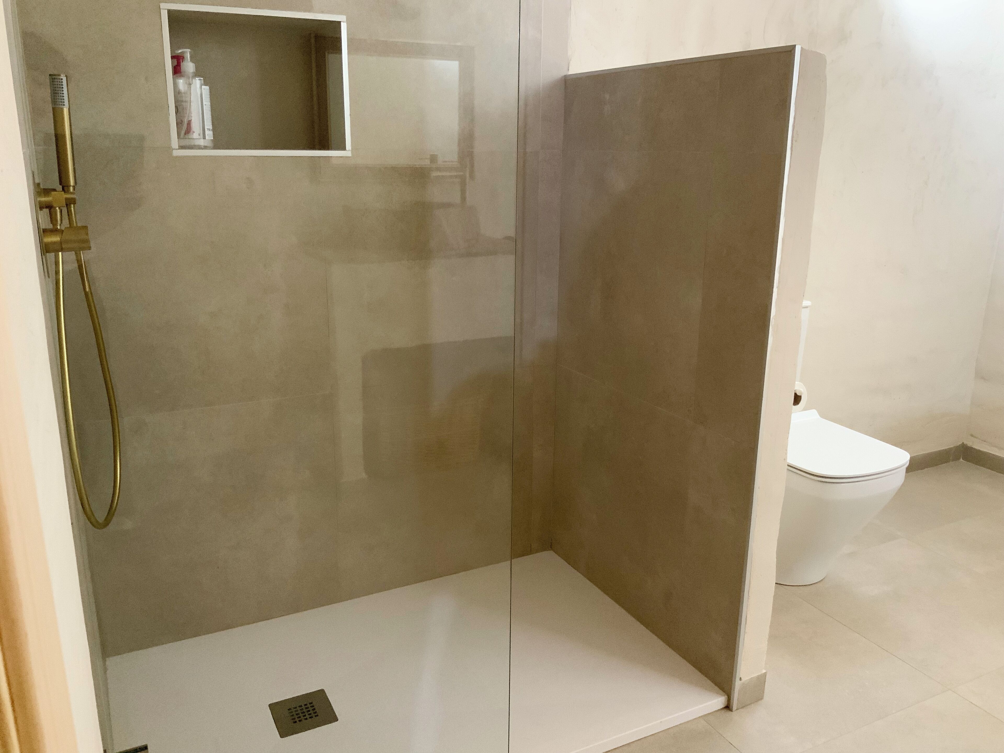 Une salle de bain moderne avec une douche à parois de verre, des toilettes et une petite étagère contenant des articles de toilette.