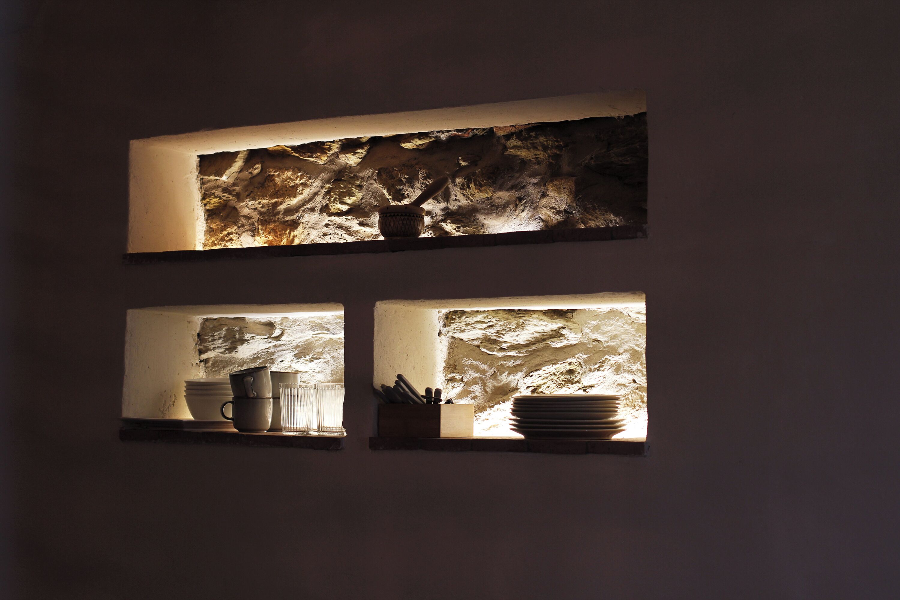 Una cocina con dos estantes iluminados que exhiben utensilios y vajilla.