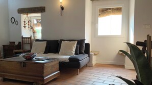 A cozy living room with a wooden coffee table, a sofa with cushions, a small side table, and a window with a woven blind. - La Grulla Dorada (Perales del Puerto)