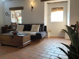 Una sala de estar acogedora con una mesa de centro de madera, un sofá con cojines, una pequeña mesita auxiliar y una ventana con una persiana tejida.