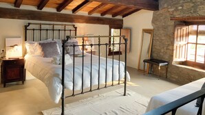 A bedroom with a wooden ceiling, a metal bed frame, a stone wall, and a window with shutters. - La Grulla Dorada (Perales del Puerto)