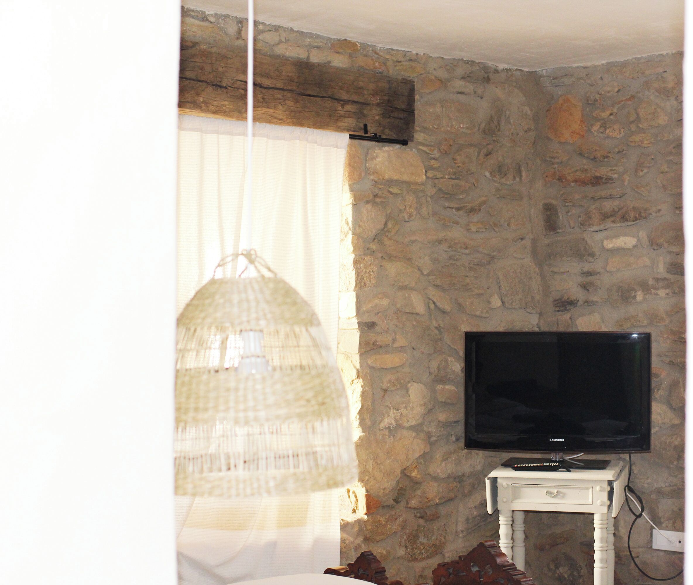 A room with a stone wall, a television on a white table, and a hanging light fixture.