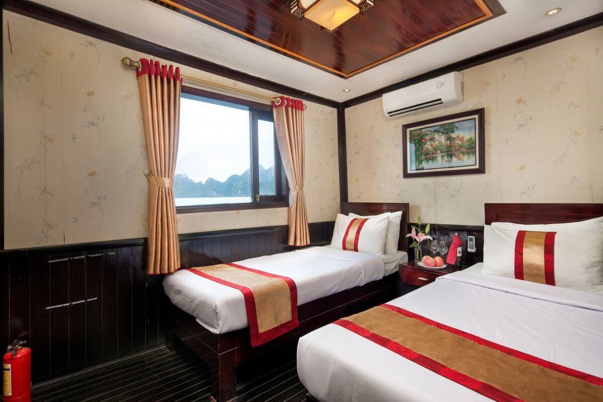 A hotel room with two beds, a window with curtains, an air conditioner, and a painting on the wall.