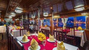 Un restaurant où les tables sont dressées pour le dîner, avec des serviettes jaunes, des verres à vin et un vase rempli de fleurs jaunes.