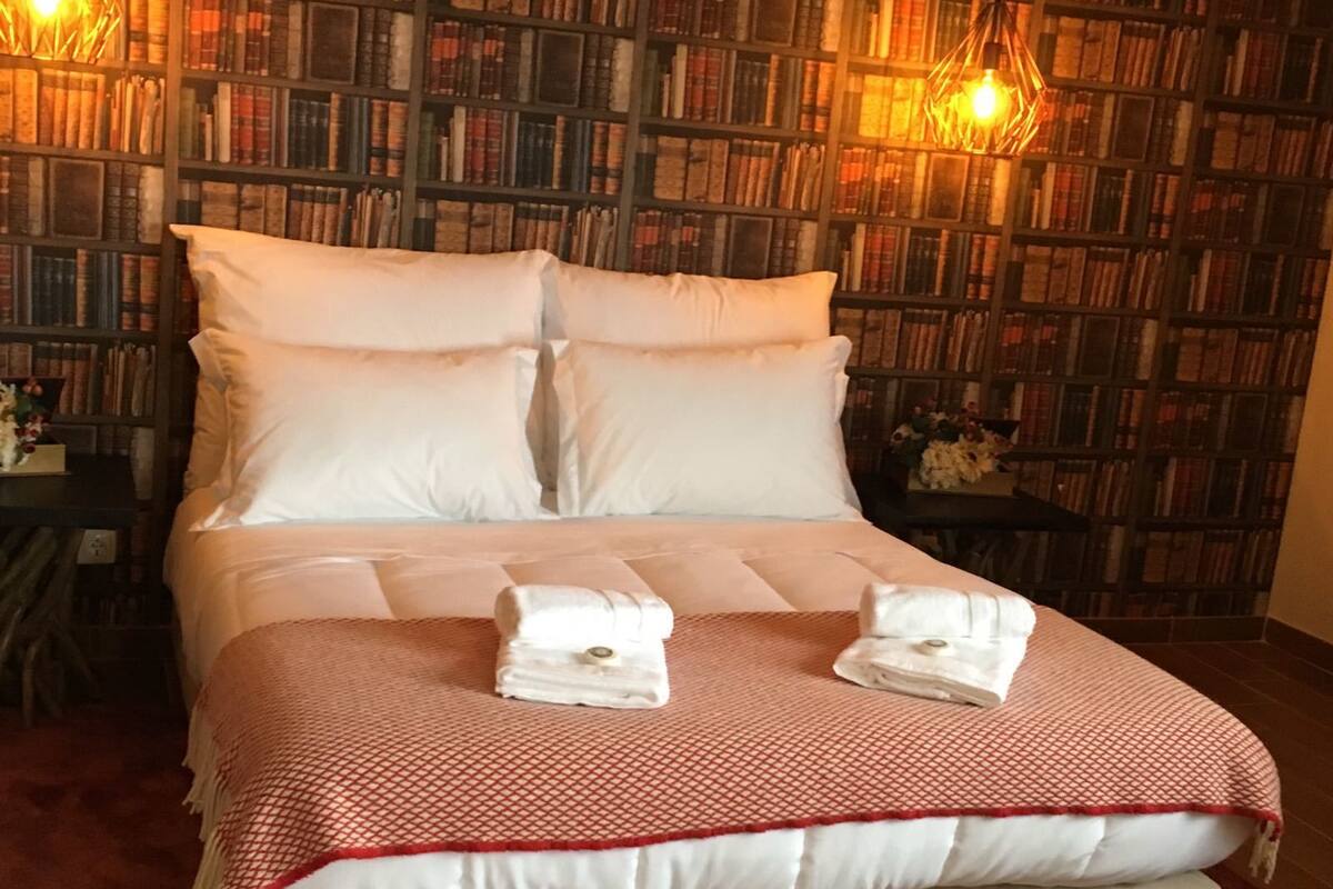 Uma cama bem arrumada com colcha xadrez vermelha e branca, duas almofadas e duas toalhas dobradas sobre a cama.