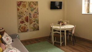 A room with a dining table, chairs, a sofa, a TV mounted on the wall, and a window. - Casa Aldeia da Lapa (Sernancelhe)