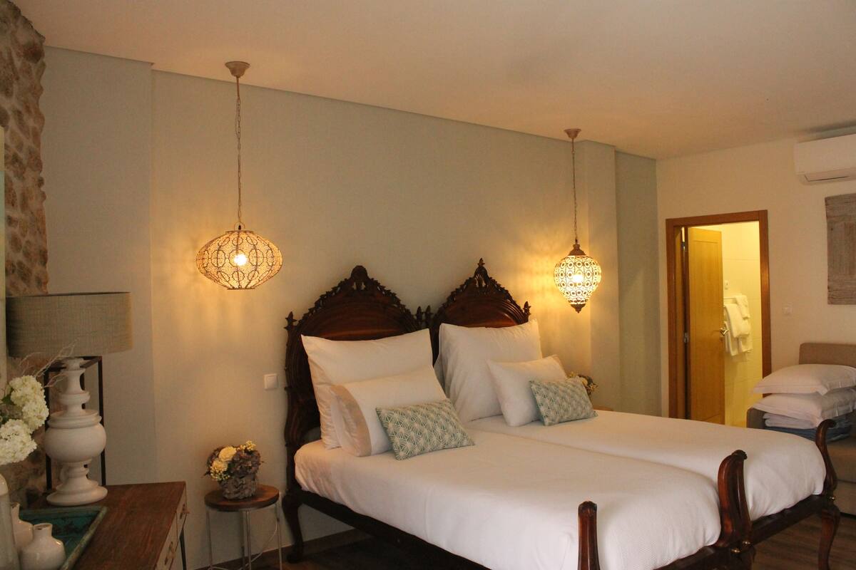 Uma cama de casal com cabeceira de madeira, duas luminárias de apoio e uma pequena mesa com um vaso de flores.