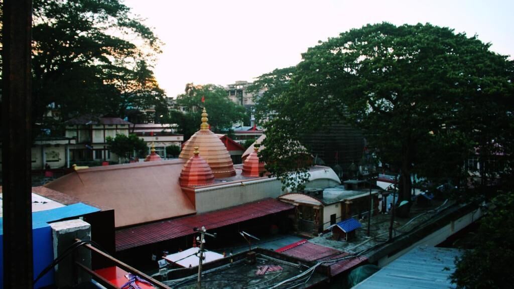 Un templo con techo rojo y dos agujas doradas, rodeado de árboles y edificios.