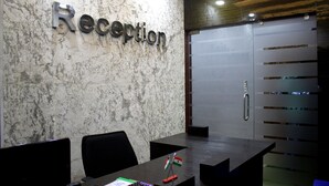A reception area with a marble wall, a reception desk, two chairs, and a door with a push bar.