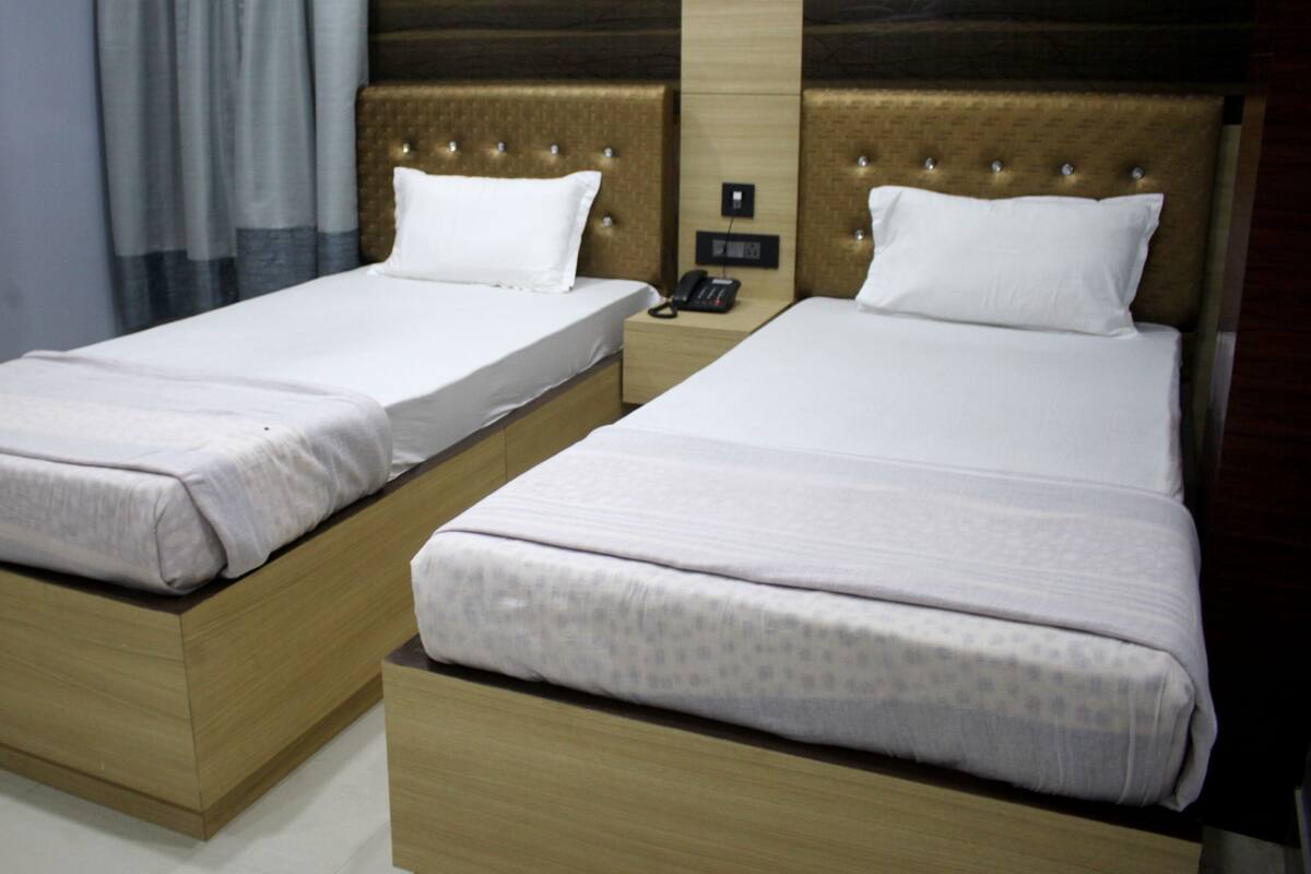 Dos camas individuales con cabeceras de madera y sábanas blancas en una habitación de hotel.