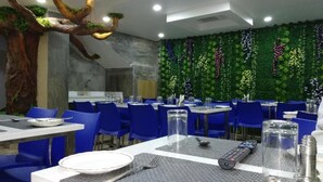 A restaurant with blue chairs, white tables, and a green wall with plants.