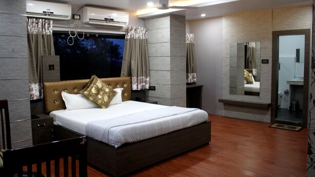A modern hotel room with a large bed, a wooden floor, a built-in TV, and a large mirror.