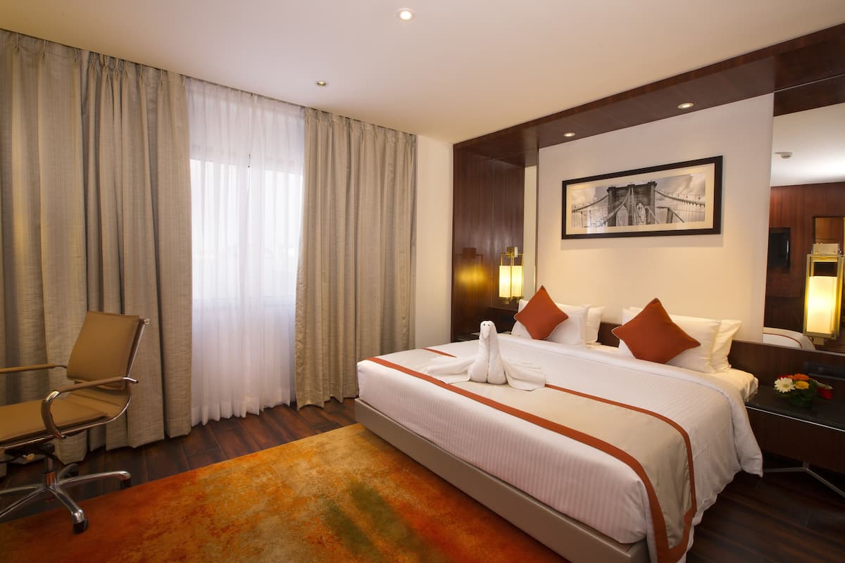 A hotel room with a large bed, a chair, a desk, and a painting on the wall.