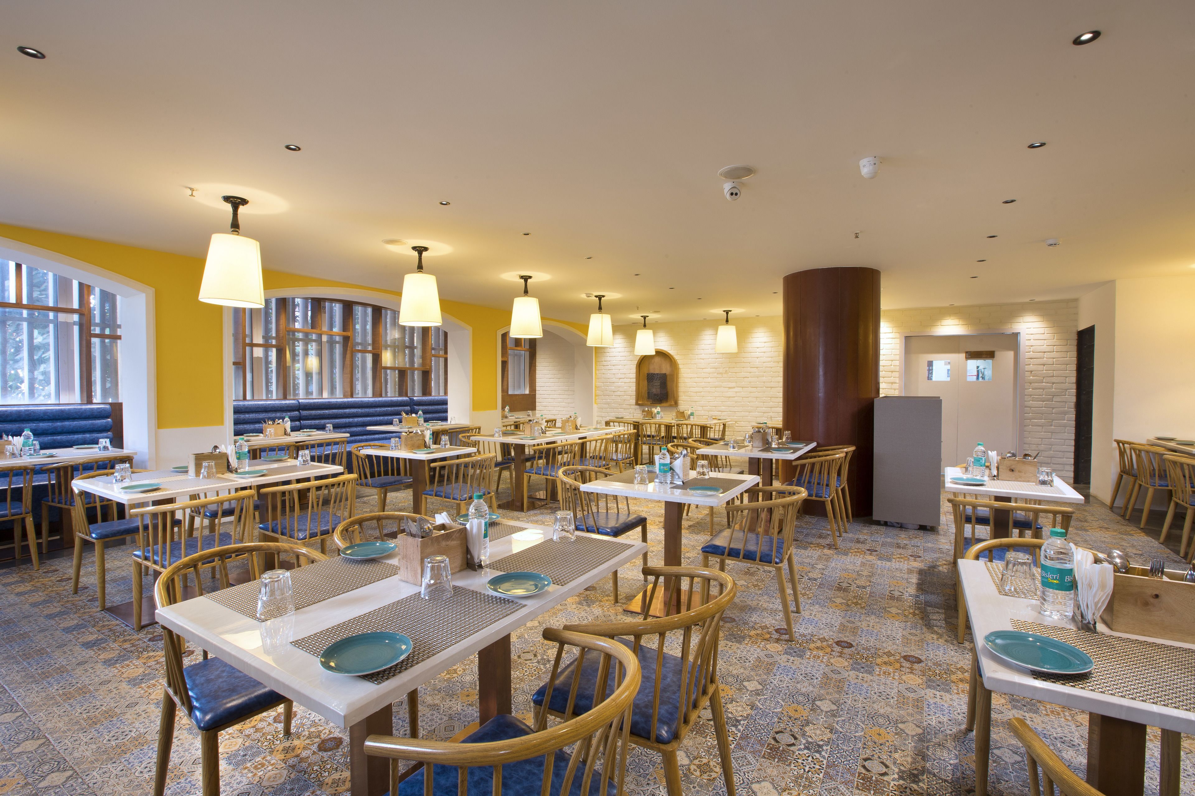 Un espace repas comprenant plusieurs tables et chaises, dont certaines sont dotées de coussins bleus, et un sol à motifs.