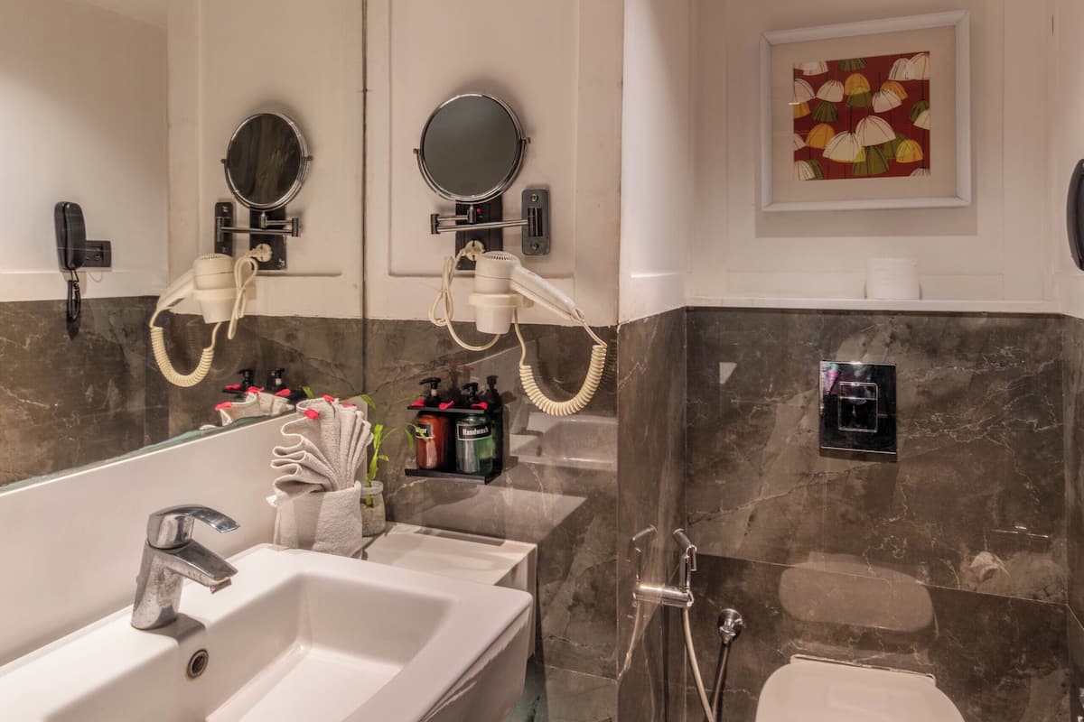 A modern bathroom with a large mirror, two sinks, a toilet, and a shower.
