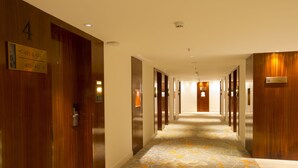 Corredor de hotel com portas de madeira, placas com números e um tapete estampado.