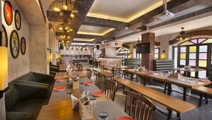 Restaurante com várias mesas e cabines de jantar, área de cozinha ao fundo, e design de interiores moderno.