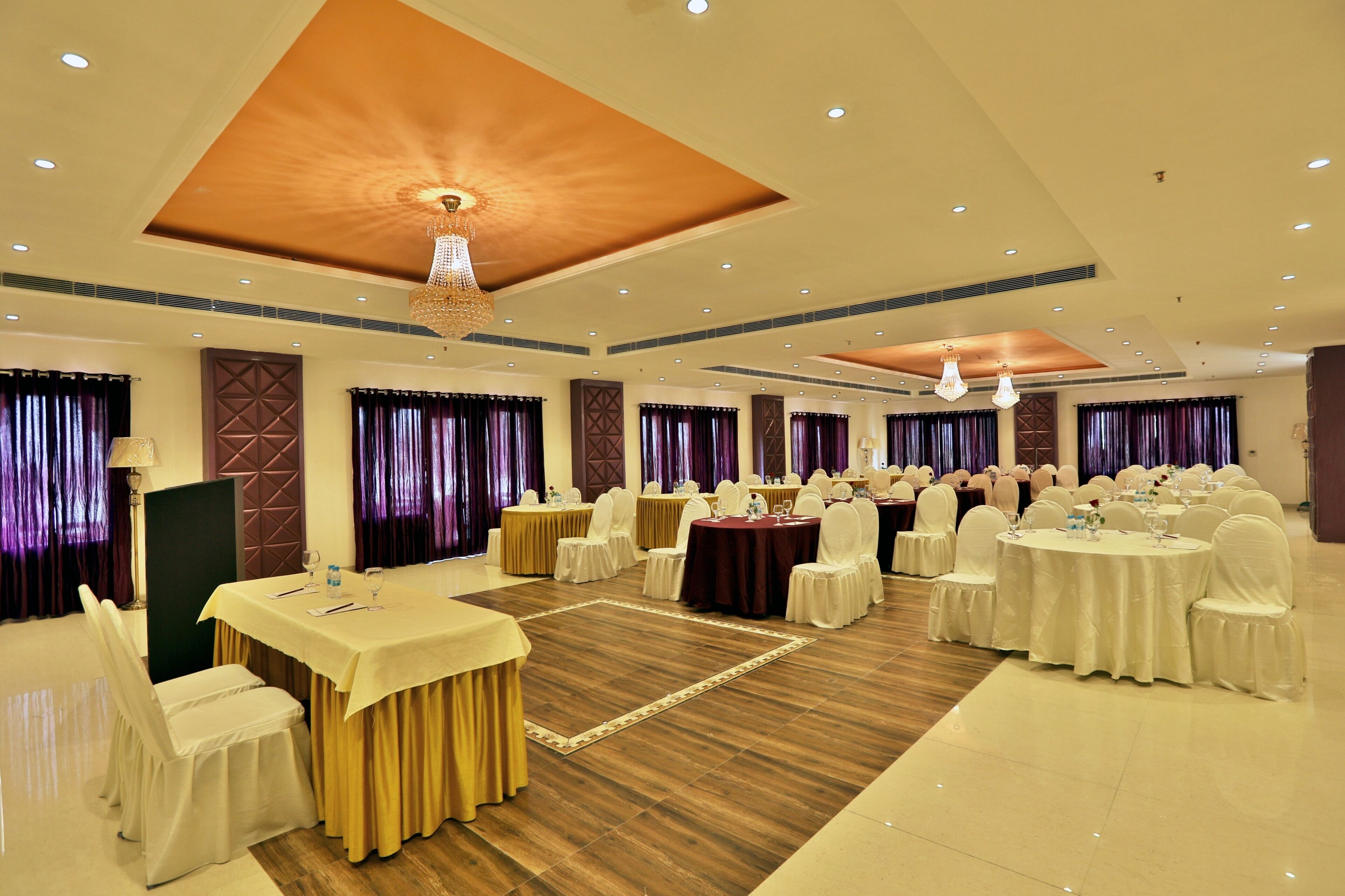 A banquet hall with round tables, white chairs, and a chandelier.