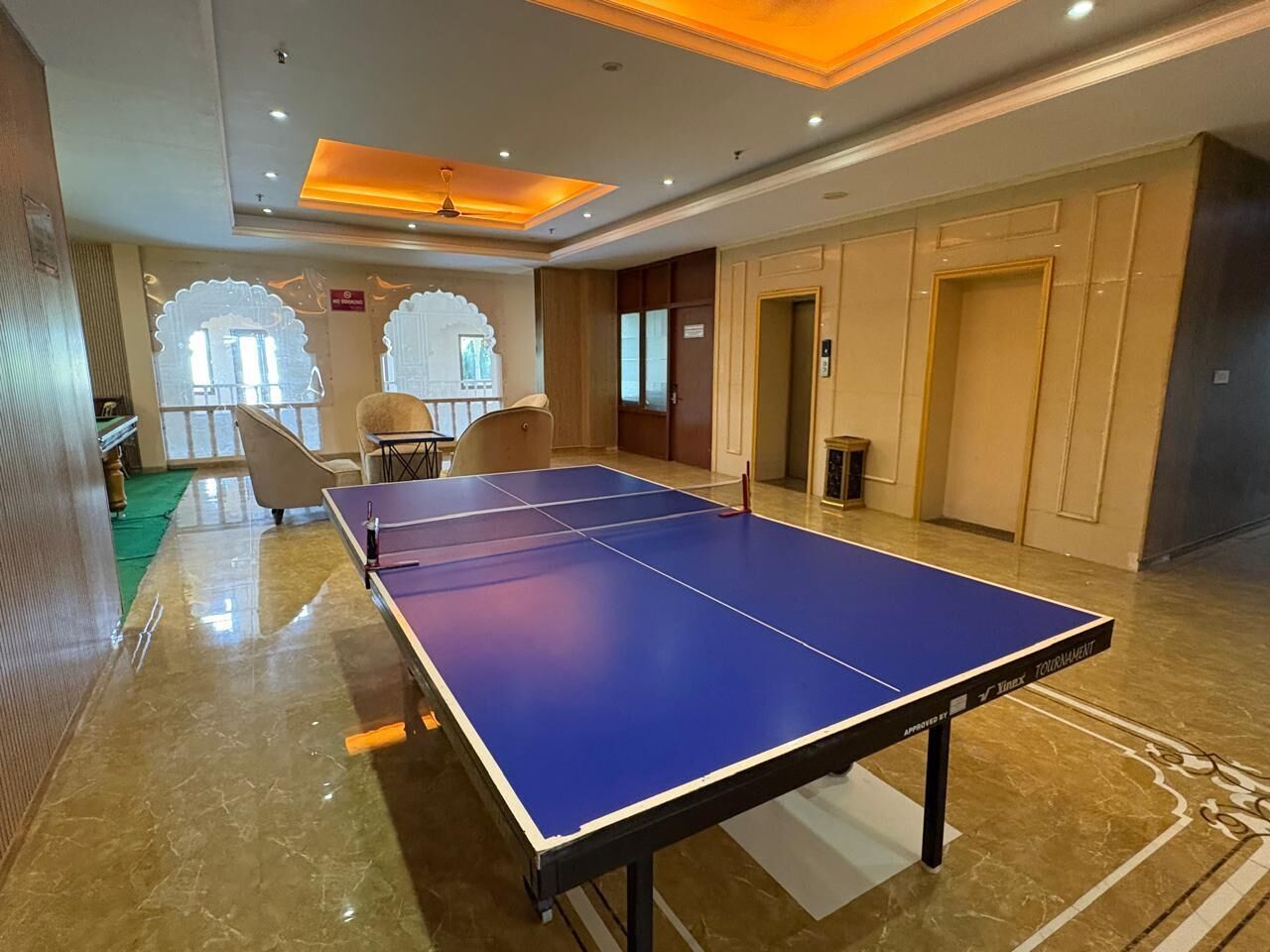 A ping pong table in a room with a marble floor, a ceiling fan, and a door in the background.
