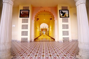 A corridor with patterned flooring, white columns, and framed pictures on the walls.