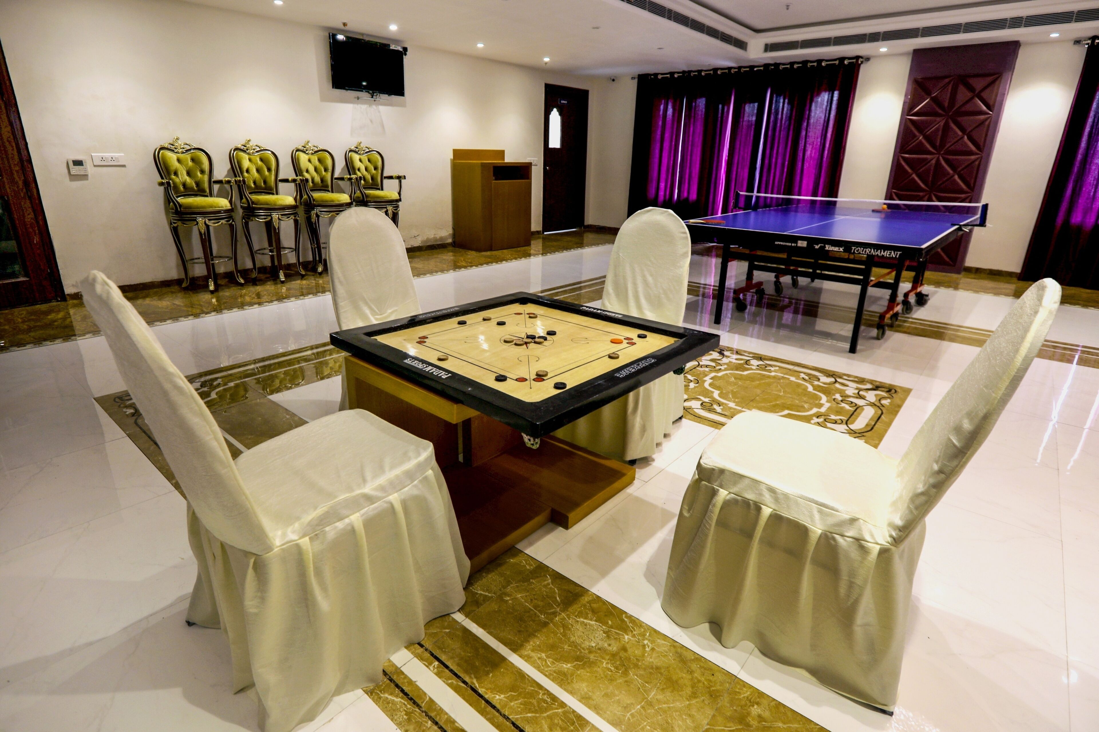 Una mesa de billar rodeada de cuatro sillas, una mesa de tenis de mesa y un atril en una habitación con suelo de baldosas y cortinas moradas.