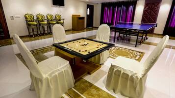 A billiards table surrounded by four chairs, a table tennis table, and a podium in a room with a tiled floor and purple curtains.