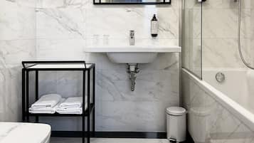 Un baño moderno con pared de azulejos de mármol, un lavamanos blanco, toallero negro, inodoro y zona de ducha.