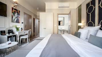 Een hotelkamer met een bed, een bureau met stoel, een klein tafeltje met dienblad, een televisie en een schilderij aan de muur.