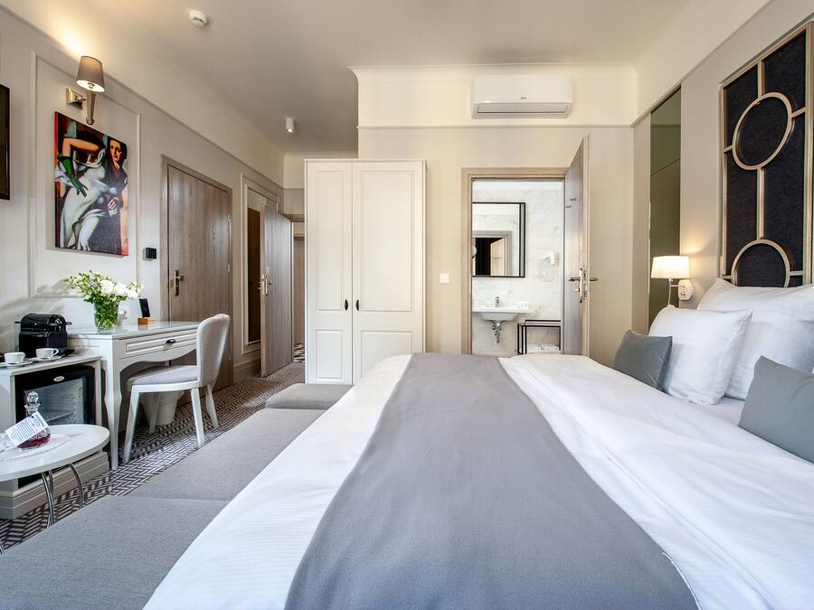 Een hotelkamer met een bed, een bureau met stoel, een klein tafeltje met dienblad, een televisie en een schilderij aan de muur.