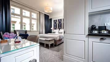 Quarto de hotel com cama, escrivaninha com cadeira, mesinha de cabeceira com abajur e vista para o exterior através de grandes janelas.