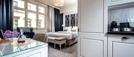 Habitación de hotel con cama, escritorio con silla, una mesita con lámpara y vistas al exterior a través de amplias ventanas.