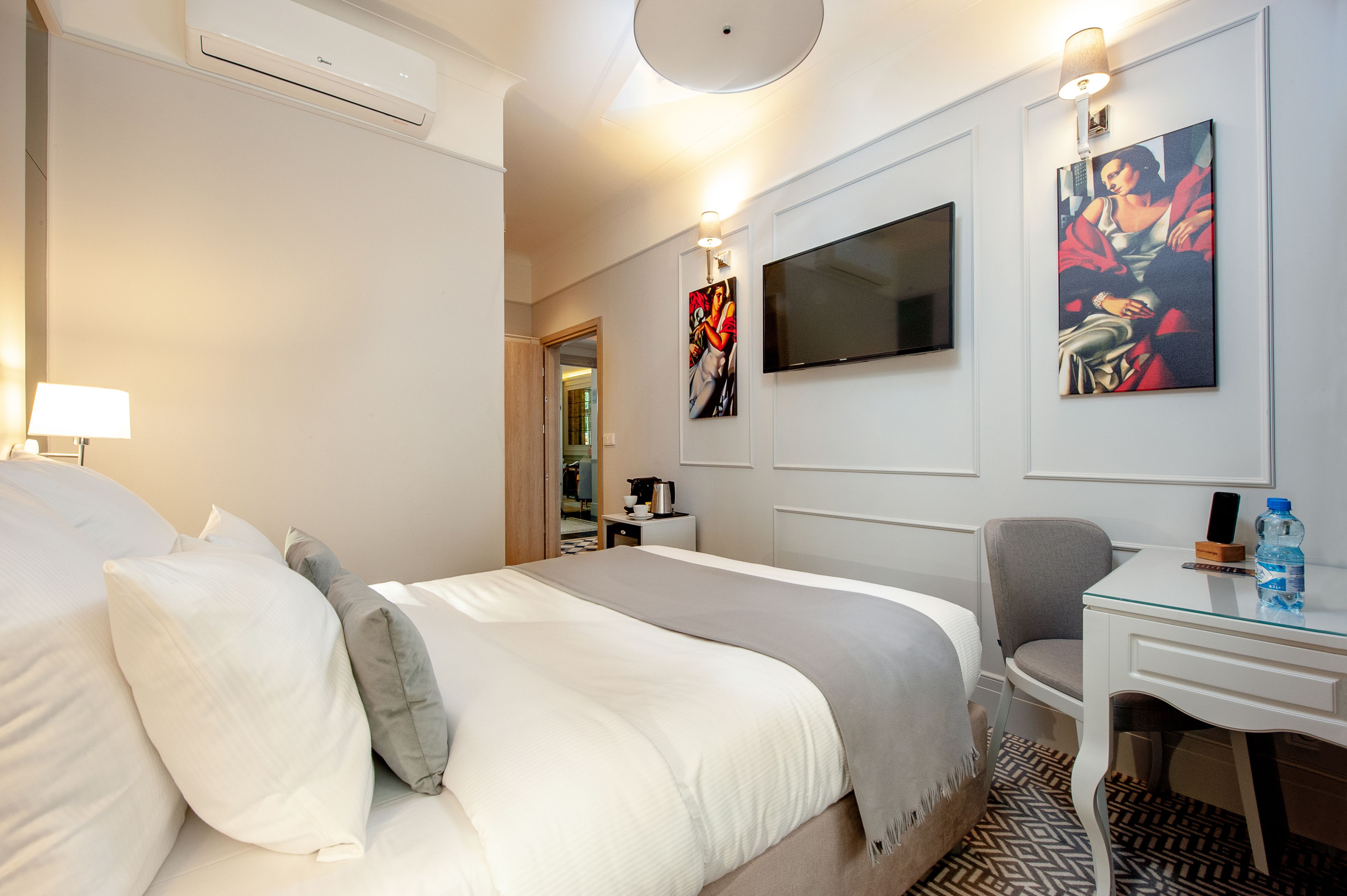 Une chambre d’hôtel dotée d’un grand lit, d’un bureau avec une chaise, d’un téléviseur à écran plat et d’œuvres d’art accrochées aux murs.