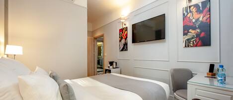 Una habitación de hotel con cama, escritorio, silla, televisor y obras de arte en las paredes.
